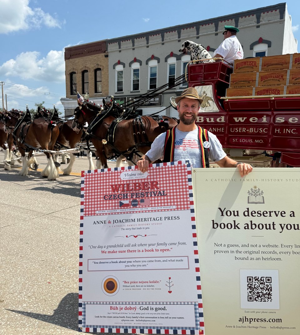 Daniel Dobesh smiles while holding two display panels as a horse-drawn red wagon passes behind him at the 2026 Wilber Czech Festival.